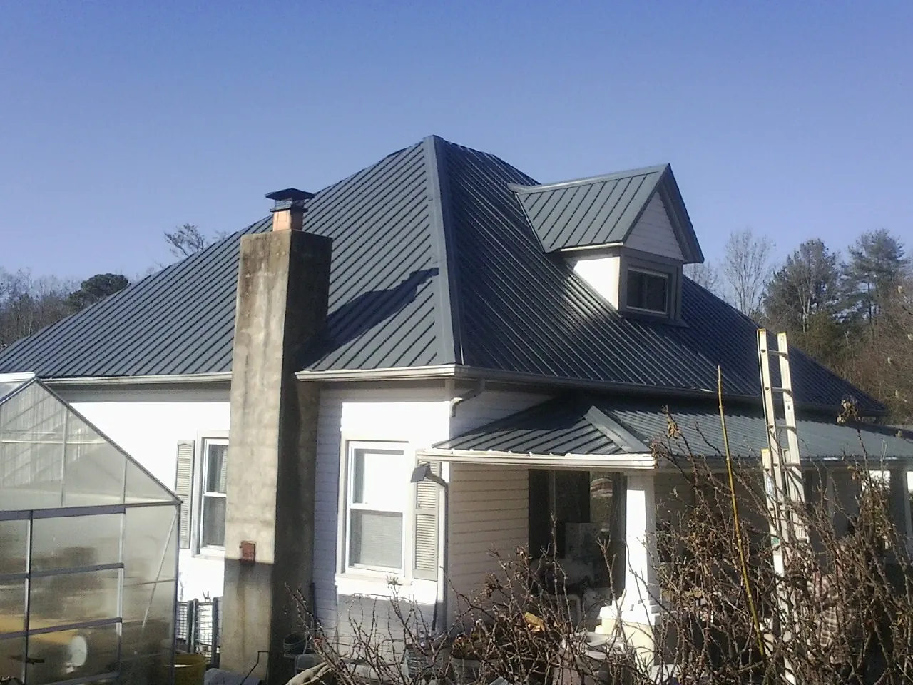 Dark blue standing seam metal roof on a white farmhouse with dormer — Slate & Tile Roof Repair by Roofing Brothers in Elrod