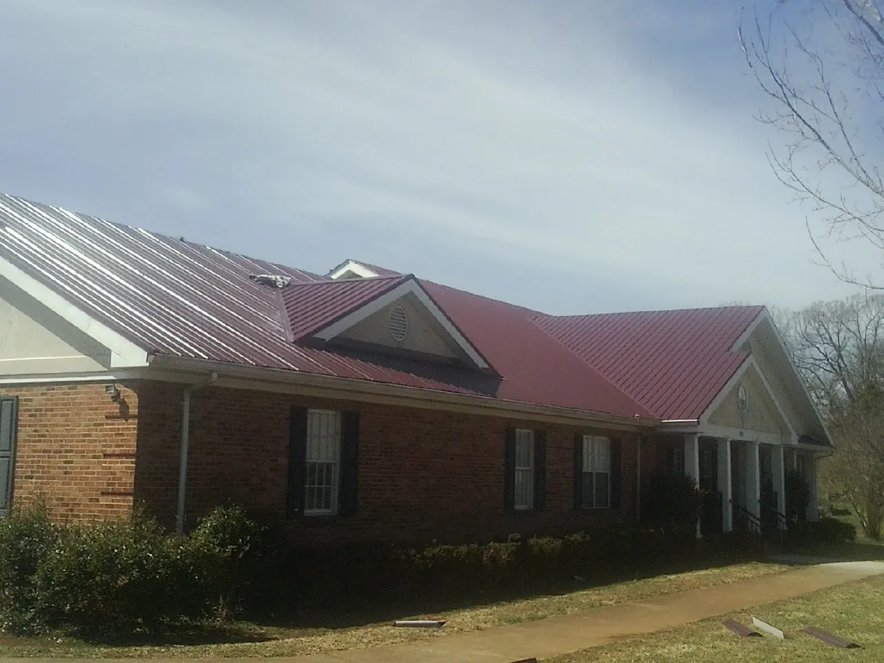Red metal roof with gabled entries on a long brick building, from a Hail Damage Roof Repair job in Elrod