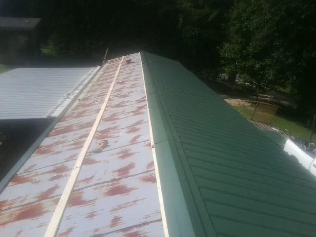 Old rusted panels beside newly installed green metal roofing — Wind Damage Roof Repair by Roofing Brothers in Elrod