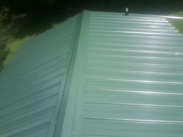 New green metal panels meeting at the ridge of a roof — Flat Roof Repair work by our crew in Elrod