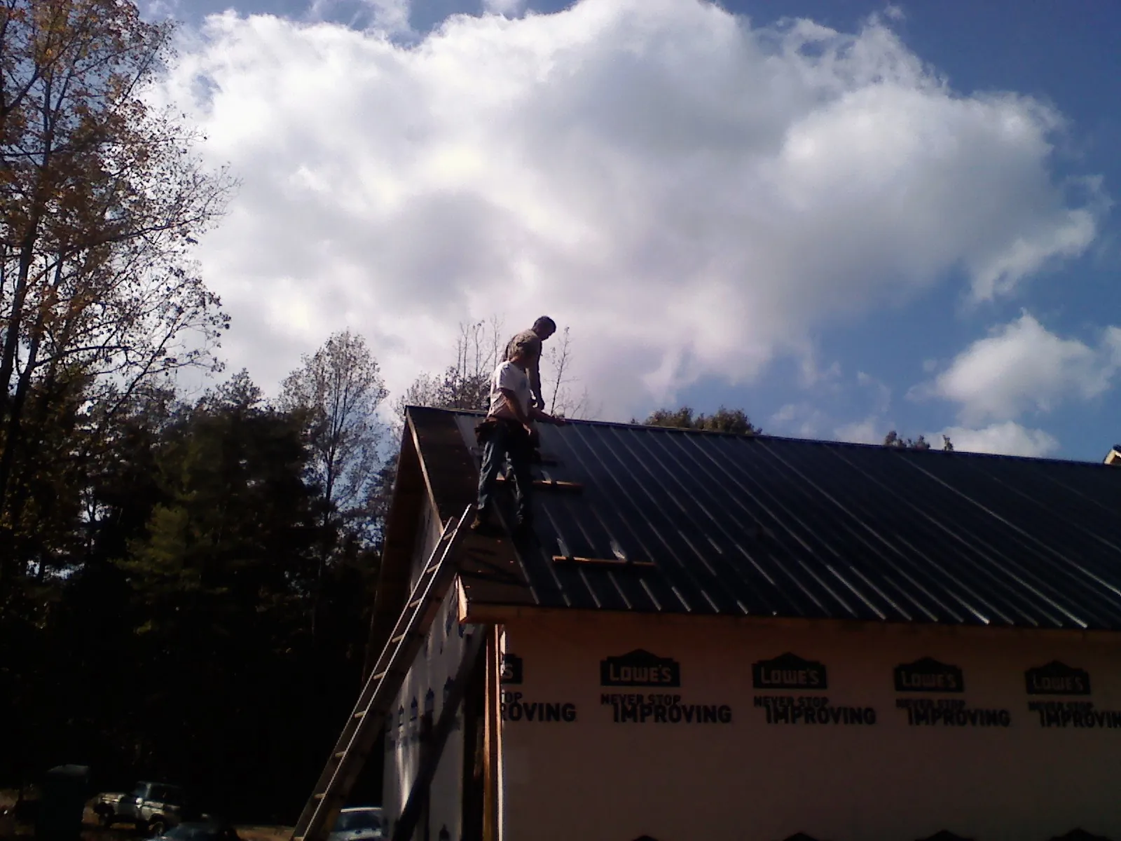 Roofer fastening dark metal panels high against a cloudy sky, from a Roof Inspection job in Elrod