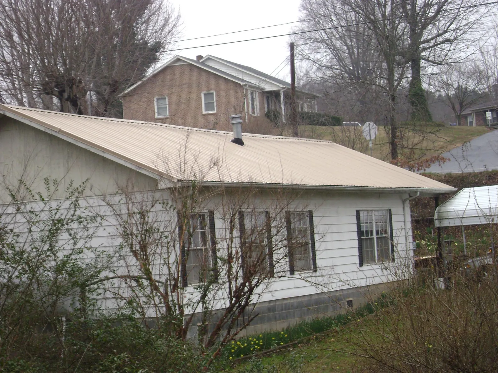 Tan metal roof on a white sided house set into a hillside — Commercial Roofing by Roofing Brothers in Elrod