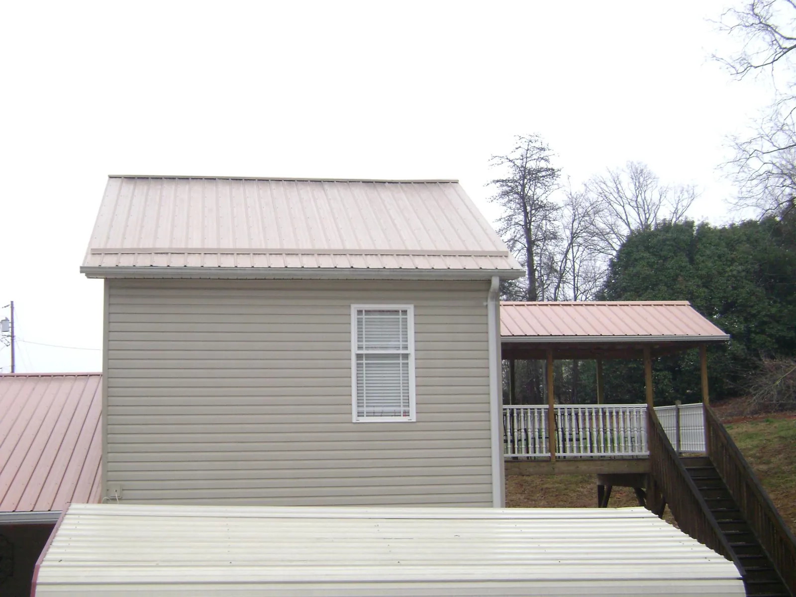 Tan metal roofs on a two story addition and attached porch, from a Roof Replacement job in Elrod